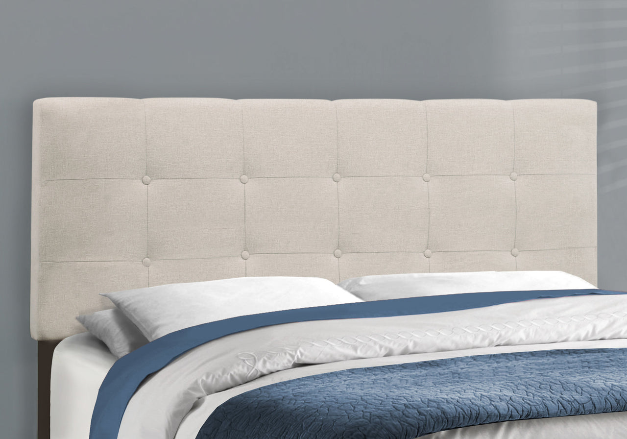 Beige upholstered headboard with bedding on a bed against a gray wall