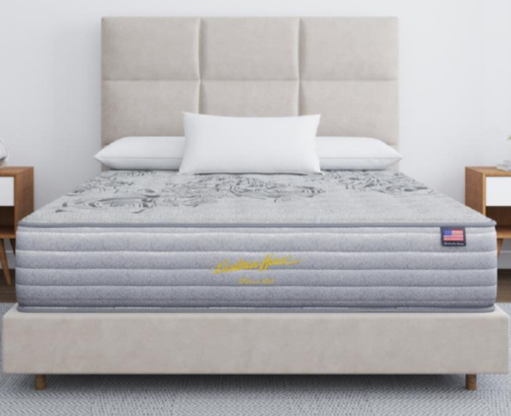 Gray mattress on a bed with a beige headboard and pillows in a room setting.